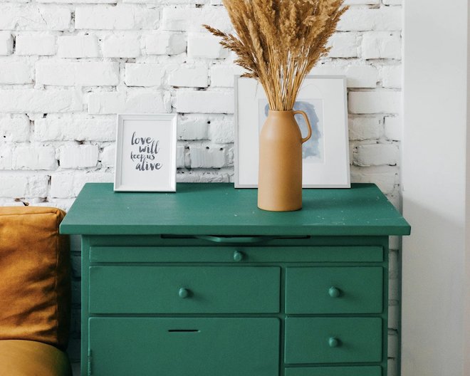 A vintage green solid wood side table decorated with two portraits and a vase of dry natural elements.